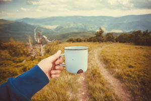 Person's hand raising a mug of hot drink with hills in the background